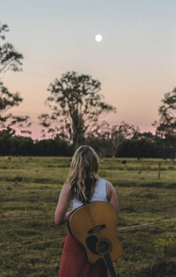 Woman with guitar in field at dusk